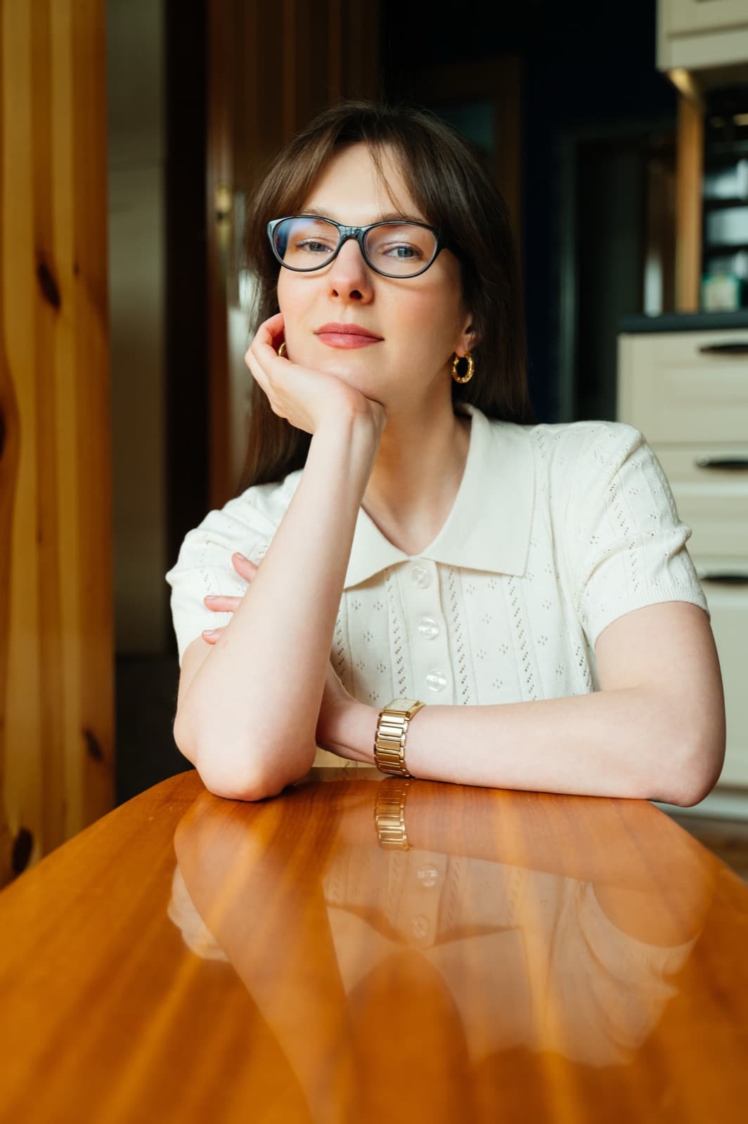 Agata Myśliborska-Błyskun w okularach, oparta o drewniany stół, patrzy w bok